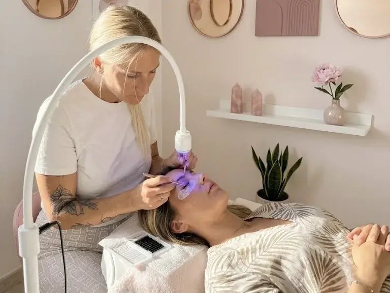 Alicia pose des extensions de cils sous la lampe LED, dans son salon de Grasse